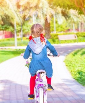 Little girl riding on the bicycle, back side, active childhood, cute little cyclist, summer vacation, healthy lifestyle, happy cycling concept