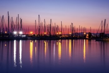 Harbor in the evening, silhouettes of luxury sailboat moored in the port, beautiful view on yachts with many glowing lights, active summer vacation