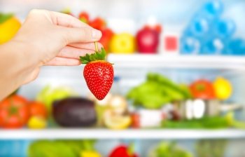 Eating healthy food conceptual background, weight loss and body care concept, fresh strawberry in hands, full fridge of diet nutrition, selective focus
