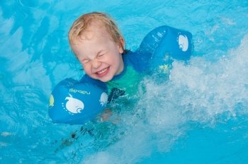 Young child swimming with arm bands and being splashed