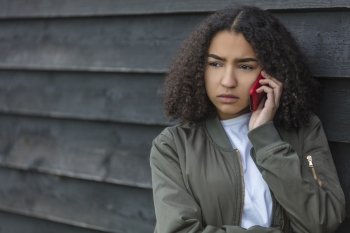 Outdoor portrait of beautiful sad aggressive mixed race African American girl teenager female young woman talking on red cell phone wearing green bomber jacket