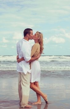 Instagram style photograph of romantic young man and woman couple embracing and kissing on a beach 