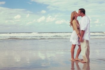 Instagram style photograph of romantic young man and woman couple holding hands and kissing on a beach 