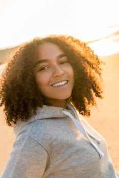 Outdoor portrait of beautiful happy mixed race African American girl teenager female young woman on a beach smiling laughing with perfect teeth in golden sunset evening sunshine