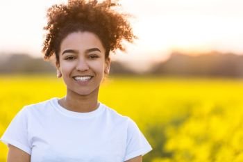 Outdoor portrait of beautiful happy mixed race African American girl teenager female young woman smiling with perfect teeth in a field of yellow flowers