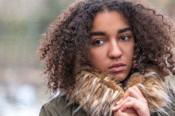 Beautiful mixed race African American girl teenager female young woman outside wearing fake fur collar coat looking sad depressed or thoughtful