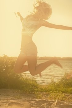 Carefree woman jumping in the sunset light on the beach. Vacation happy living concept retro color shot copyspace. Carefree woman jumping in the sunset light on the beach. Vacation happy living concept retro color shot with copyspace.