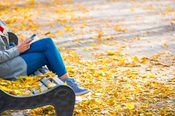 Young woman sitting on a bench in autumn park with yellow fallen leaves