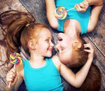 Fine portrait of a twin sisters holding colorful  lollipops