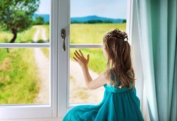 Little sad girl looking through window