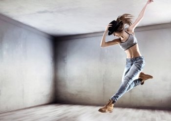 Athletic young dancer jumping on a concrete wall background