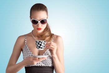 A photo of pin-up girl in spotted dress and sunglasses holding a cup.