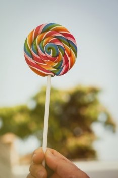 Caucasian hand holding a round lollipop with many colors in a spiral