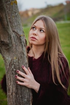 Portrait blonde girl next to a tree trunk in a park 