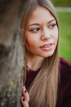 Portrait blonde girl next to a tree trunk in a park 