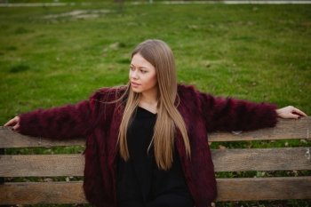 Pretty blonde girl with fur coat sittig in a bench in the park 