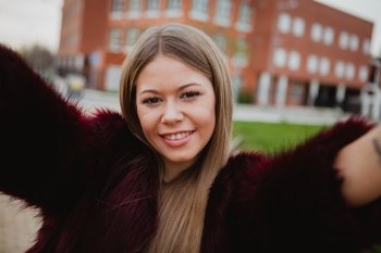Pretty blonde girl with fur coat in the park making herself a photo