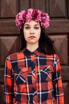 Pretty stylish girl with pink flower crown and red plaid shirt In front of a wooden door