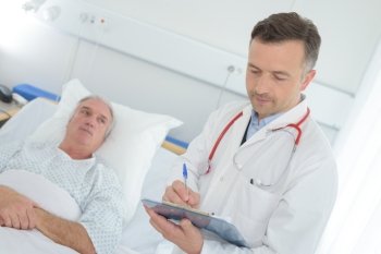 doctor with clipboard visiting senior patient at hospital ward
