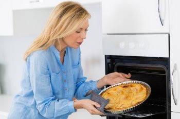 mature blond woman baking tart in oven