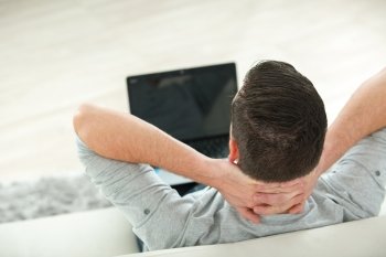 young man lying on sofa watching video on laptop