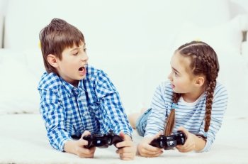Kids playing game console. Emotional kids lying on floor playing games on joystick