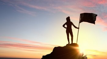Reaching top of world. Silhouette of young woman with flag on mountain top 