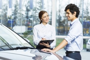 Young woman dealer in auto salon presenting car to customer. This car is perfect for you
