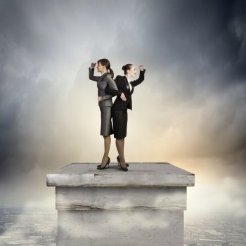 Business perspective. Image of two businesswomen looking into distance standing back to back