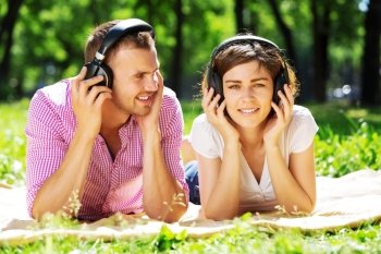 Loving young couple in summer park listening music. Weekend in park
