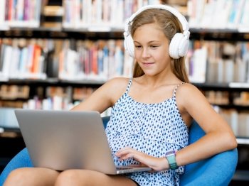 A teenage girl with headphones sitting with a laptop. Browsing with music