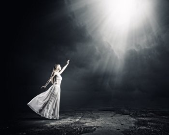 Woman in white. Young woman in white long dress reaching to light