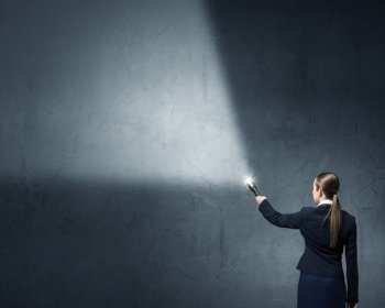 Woman with lantern in hand. Businesswoman in darkness with flashlight in hand