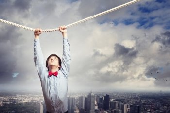 Businessman hanging on rope. Image of businessman hanging on rope against city background