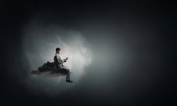 Man using his mobile phone. Young businessman sitting on black cloud with mobile phone in hands