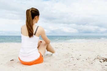 Young woman in sports wear sitting at the beach. Young woman in sports wear sitting alone at the beach and having minute of rest