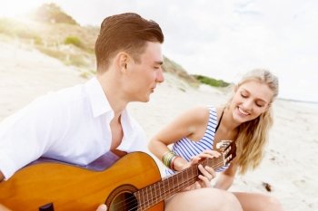 Young couple playing guitar on beach in love. Happy romantic young couple playing guitar on beach in love