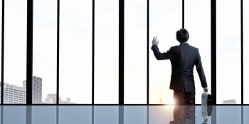 Facing next successful day. Back view of businessman looking on sunrise in office window and gesturing with hand