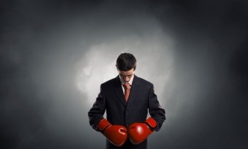 He is ready to fight for success. Young businessman in red boxing gloves on dark background