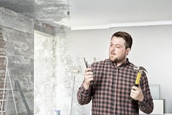 Guy with construction tools. Casual man in checked shirt indoors with hammer and nails