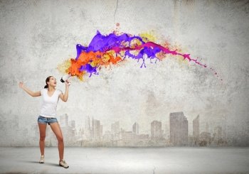 Girl with megaphone. Young woman in casual speaking in megaphone with colorful splashes flying out