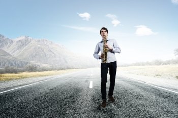 Handsome saxophonist. Young man walking on road playing saxophone 