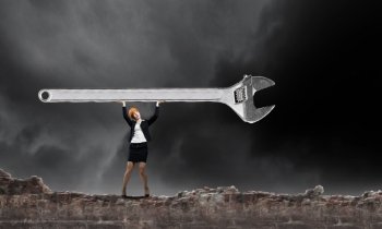 Woman engineer. Young businesswoman lifting huge wrench above head