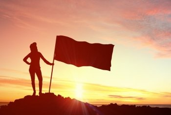 Reaching top of world. Silhouette of young woman with flag on mountain top 