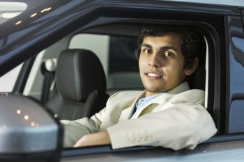 Handsome young man sitting in car in showroom . Buying car