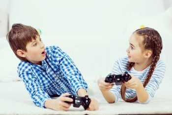 Kids playing game console. Emotional kids lying on floor playing games on joystick