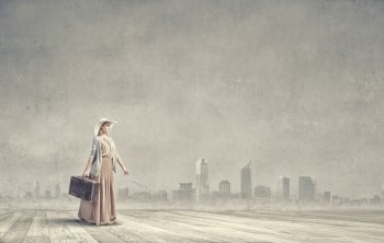 Woman with old suitcase. Beautiful woman walking with retro suitcase on cityscape background