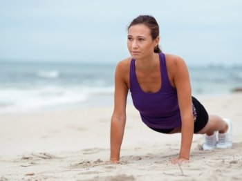 Sporty young woman doing push ups on the sea coast