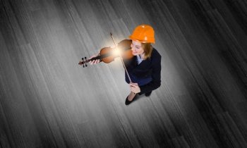 Engineer play violin. Top view of businesswoman in helmet playing violin