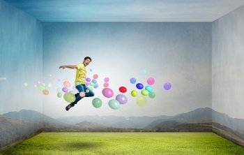 Buoyant and happy. Young man jumping in sky among colorful balloons
